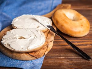A Bruegger's Bagels bagel on a slab of wood spread with cream cheese